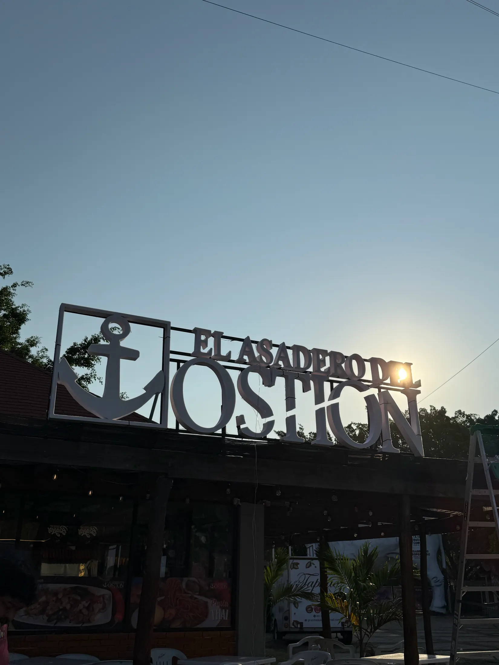 Letrero de metal recortado de El Asadero del Ostión montado sobre la palapa al atardecer