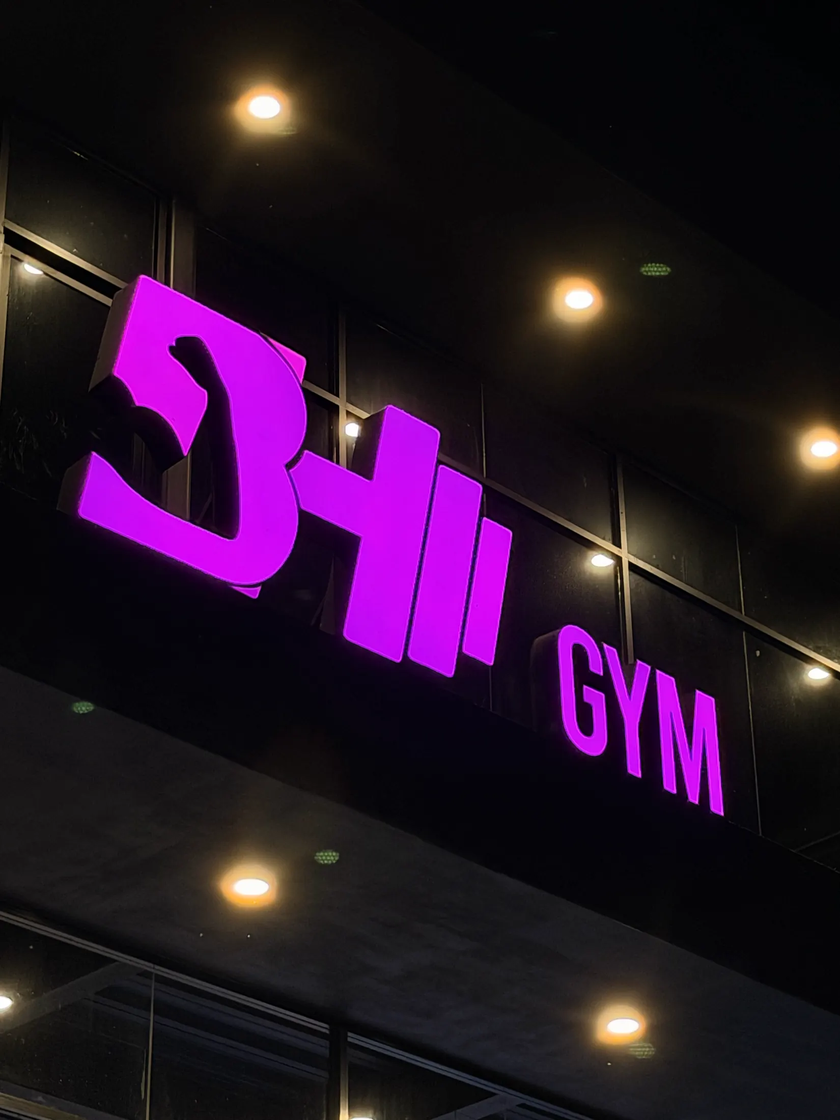 Letrero 3D retroiluminado en morado del gimnasio BH Gym sobre fachada nocturna